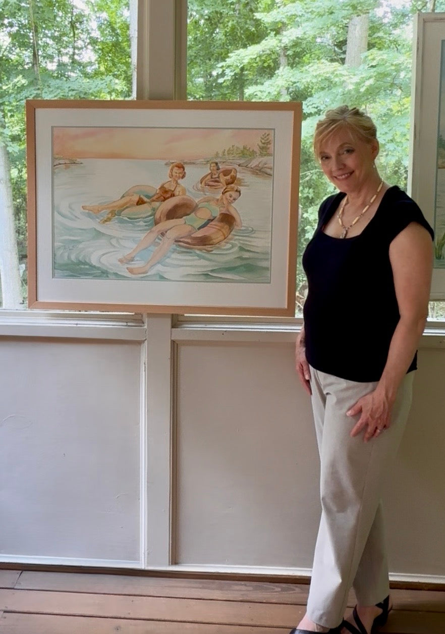 Artist Pamela Hallock standing beside her framed original figurative watercolor painting "Pink Skies," inspired by Georgian Bay and displayed in natural light.