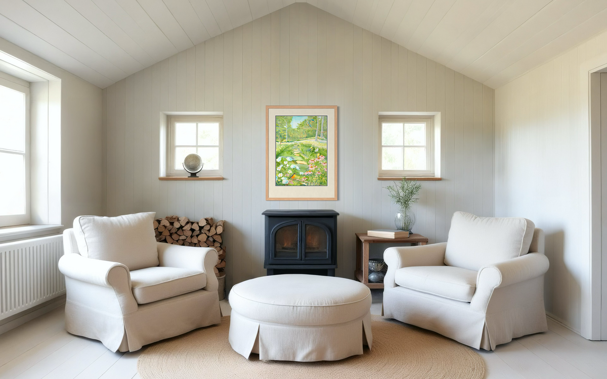 Midwest Garden watercolor print by Pamela Hallock framed above a small stove in a bright cottage sitting room with cream chairs.
