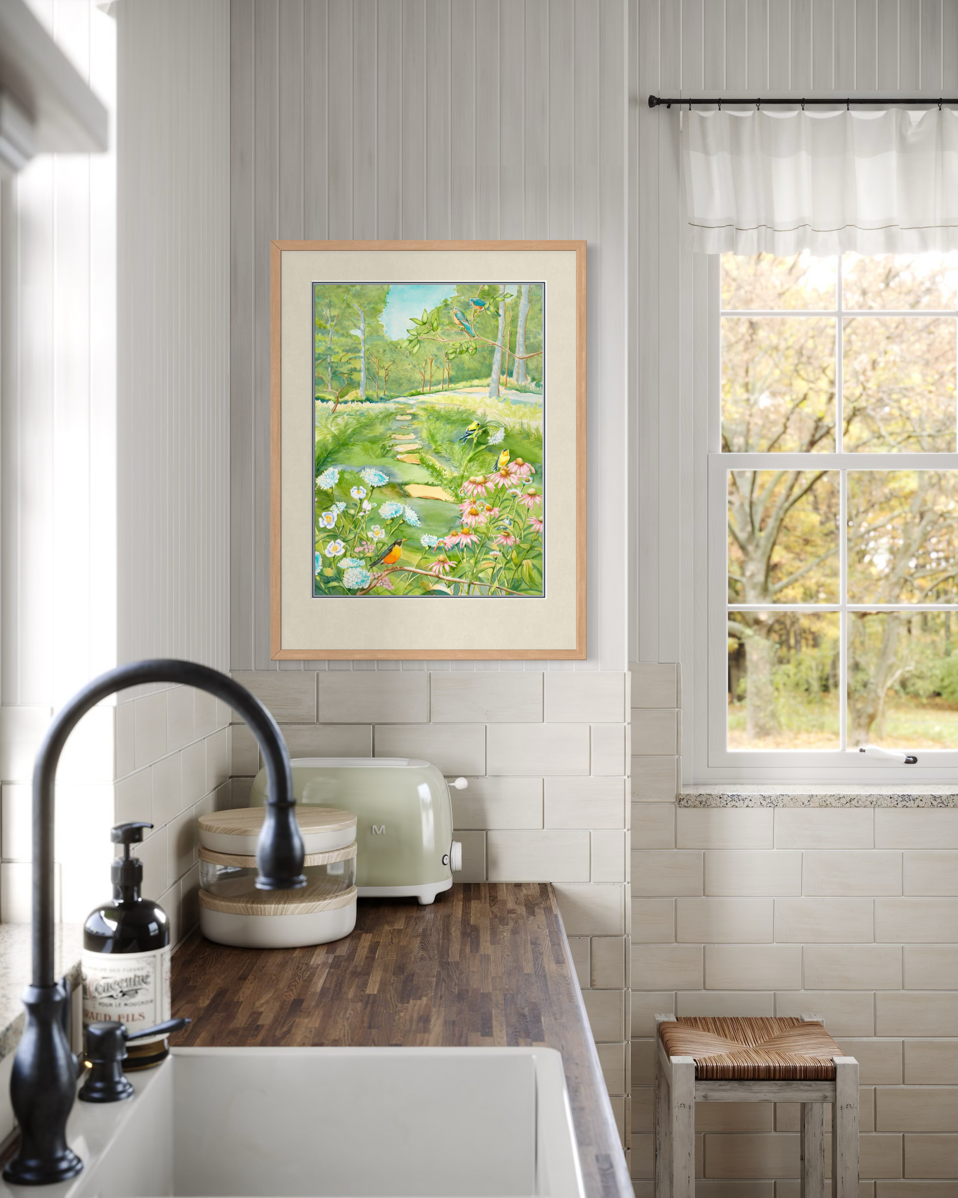 Midwest Garden watercolor print by Pamela Hallock framed in a bright cottage kitchen with white tile, warm wood counters, and garden views.