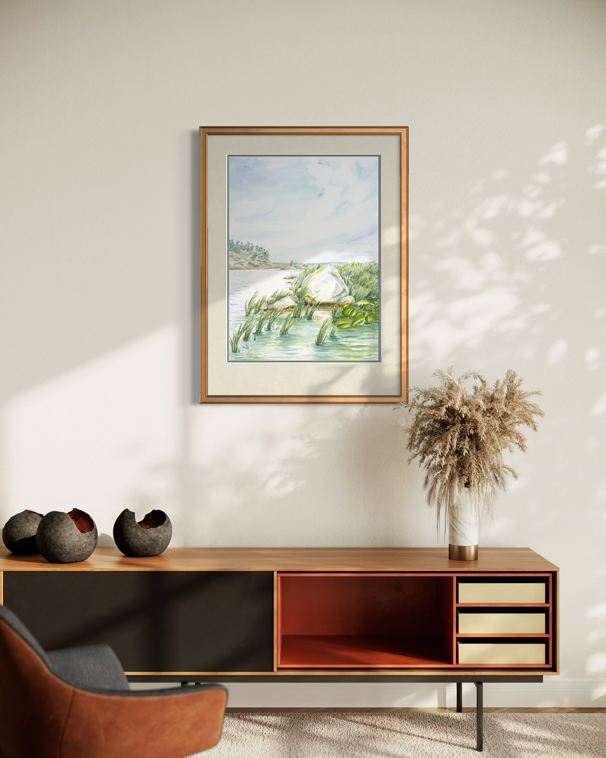 Framed Granite and Wind watercolor print of Georgian Bay shoreline displayed on a sunlit wall in a modern room.